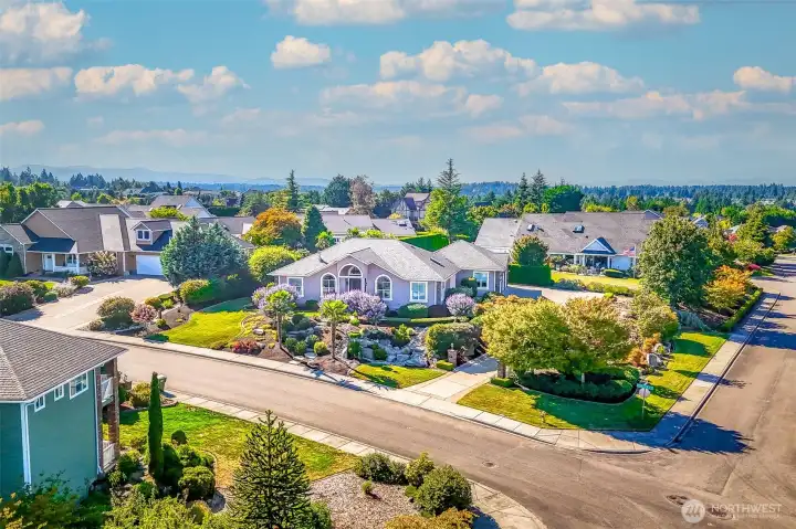 Striking aerial view showcases this elegant single-level home on a beautifully landscaped corner lot. Lush gardens, palms, and manicured beds frame the residence, creating exceptional curb appeal in a desirable neighborhood.