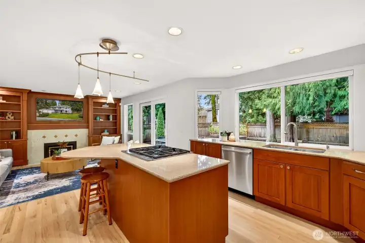 The heart of the home is a bright kitchen with expansive stone counters, a generous island with gas cooktop, and a wide window line that brings the backyard setting right into daily life.