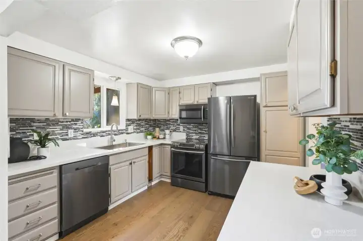 The kitchen features stainless steel appliances, solid surface countertops, and a custom tile backsplash that adds texture and visual interest.