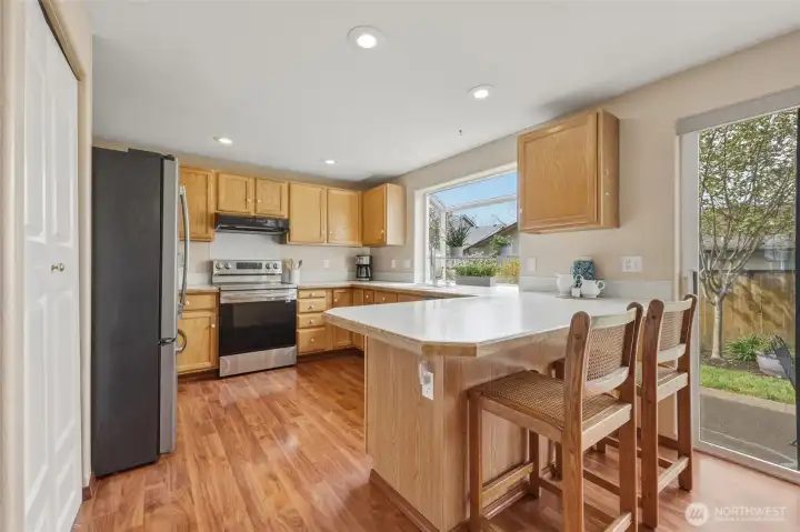 Homey and bright kitchen combines wood tones with fresh white counters and knobs, highlighting the stainless steel appliances. Eat-in bar counter is always a popular gathering/conversation spot; handy pantry seen here as well.