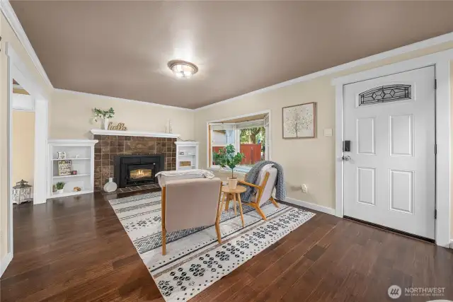 Step inside to a warm and inviting living room featuring rich engineered hardwood floors, a charming brick fireplace with insert, and built-in shelving that adds both function and character.