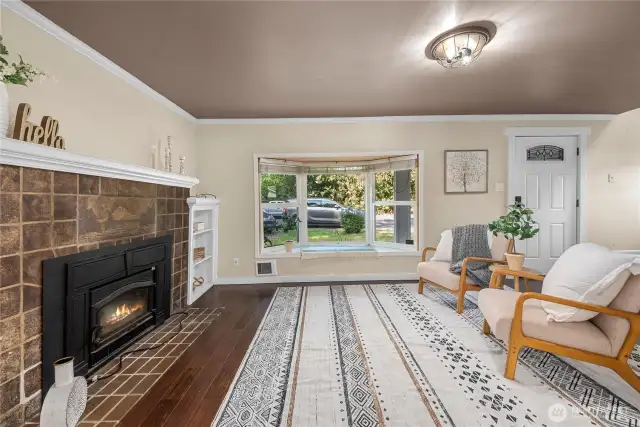 Natural light pours through the large bay window, highlighting the cozy living space and offering a peaceful view of the front yard.