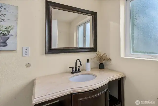 The main floor bathroom includes a spacious vanity, updated sink fixture, and framed mirror. Natural light flows in through the privacy window, brightening the space.