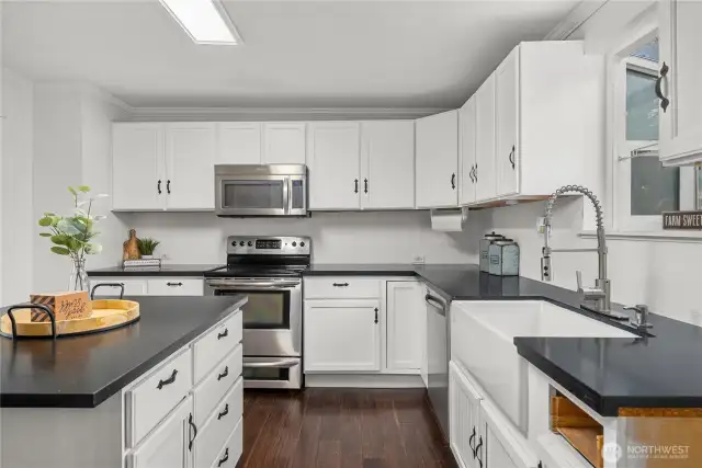 A farmhouse sink beneath the window enhances both charm and practicality, complemented by sleek counters and ample cabinet storage. The open layout ensures plenty of room for meal prep and gatherings.