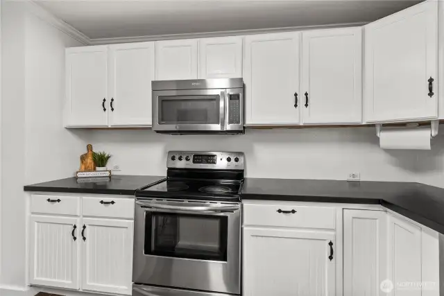 The kitchen features a modern appliance package, including a stainless steel oven and microwave, surrounded by fresh white cabinetry for a timeless, clean look.