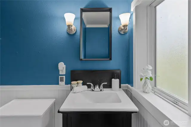 This view highlights the vanity with a sleek black base, white countertop, and matching framed mirror. Updated lighting fixtures and ample counter space make the bathroom both practical and stylish.