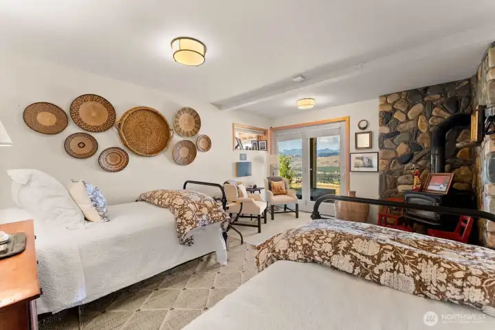 Relaxed guest bedroom 1 of two, ground level walkout daylight basement. Wood burning fireplace. Stone wall feature. Door to covered outdoor Patio and landscape mountain views.