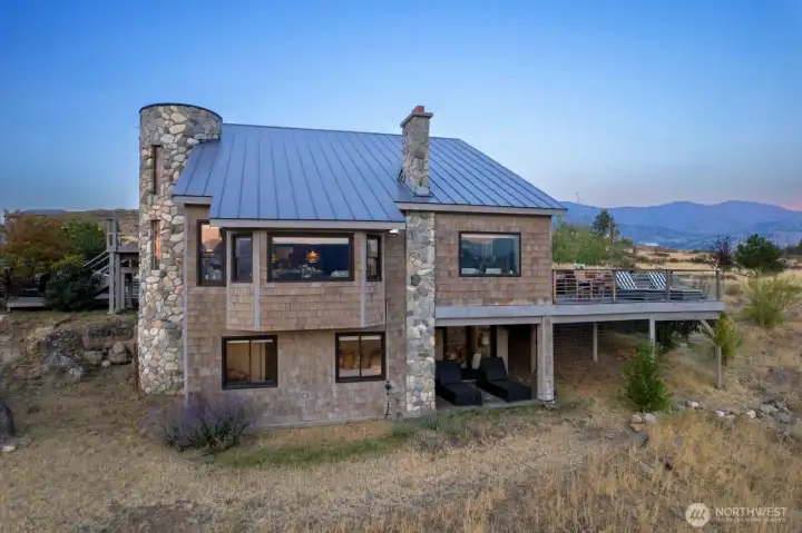 West side of the Homes artistic rock and stone crusted turret and fireplace chimney meet the cedar shake siding for a tremendous home build. Site merges with landscape perfectly.
