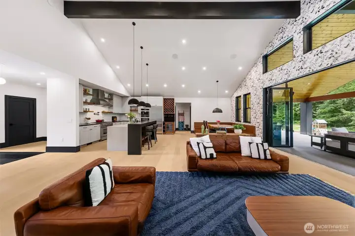 Spacious great room living and access to an all season covered deck that seamlessly flows through a window wall. Vaulted ceilings raise the space and mirror the outdoors. Custom Kitchen with designer cabinetry and shelving, Bluestar Range and Liebherr Refrigerator. Behind the wine display is a huge pantry. Primary bedroom is beyond the dining room; with direct access to the deck. To the left in this photo is the dramatic entry and hallway to the 2nd office, powder room, mud room and 3 car garage with rec room above. Spacious great room living and access to an all season covered deck that seamlessly flows through a window wall. Vaulted ceilings raise the space and mirror the outdoors. Custom Kitchen with designer cabinetry and shelving, Bluestar Range and Liebherr Refrigerator. Behind the wine display is a huge pantry. Primary bedroom is beyond the dining room; with direct access to the deck. To the left in this photo is the dramatic entry and hallway to the 2nd office, powder room, mud room and 3 car garage with rec room above.