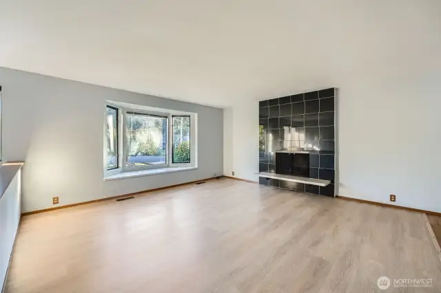 Living room filled with natural light, includes updated flooring, fireplace surround
