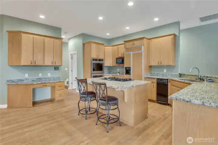 Beautiful honey-toned cabinetry paired with a built-in refrigerator and island gas cooktop with an eating bar, creating a warm and functional kitchen perfect for cooking and gathering.