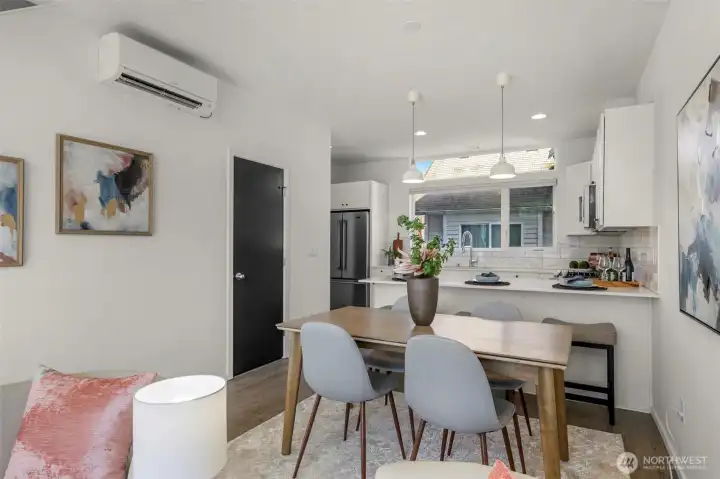 As we continue through the main level, you'll notice how the elevated ceilings create a sense of scale, comfortably accommodating both a full-sized dining table and a functional breakfast bar. The expansive windows flood the space with natural light, while the discreet door to the left provides practical understairs storage.