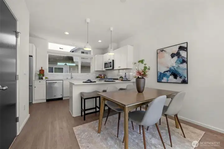 This airy open-concept space features a light-filled dining area that flows seamlessly into a gourmet kitchen with a convenient breakfast bar. Large, expansive windows flood the room with natural light, while the discreet door provides functional understairs storage.
