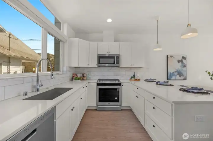 This spacious kitchen is perfectly designed for more than one cook to work comfortably, offering a functional layout with crisp white cabinetry and high-end stainless steel appliances. The open-concept design flows seamlessly into the dining area, providing plenty of room for entertaining guests in a bright and inviting atmosphere.