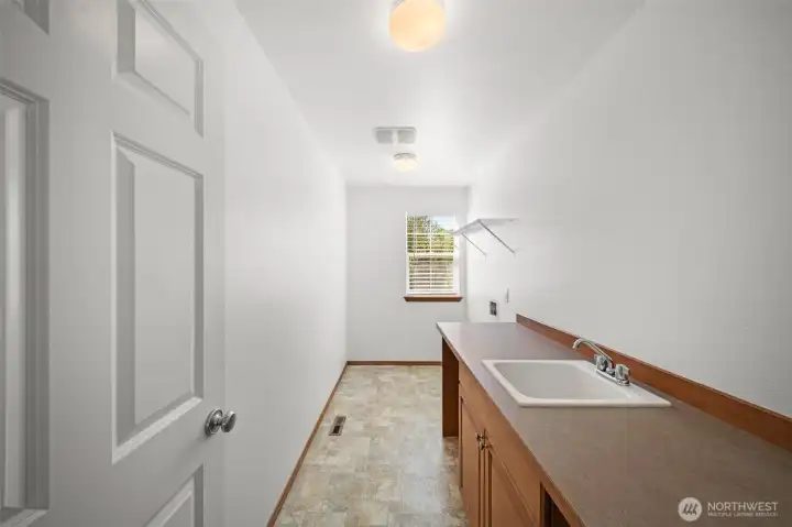 Spacious utility room for washer/dryer with a sink and storage.