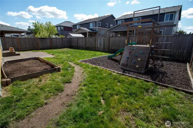 The fully fenced backyard features a patio, large garden bed & fun play set!