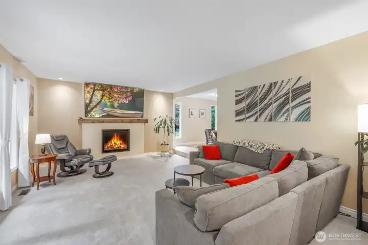 The living room is anchored by a striking fireplace with a custom mantel, perfect for cozy evenings. Expansive windows frame lush outdoor views and bring in abundant natural light, enhancing the airy feel of the room.