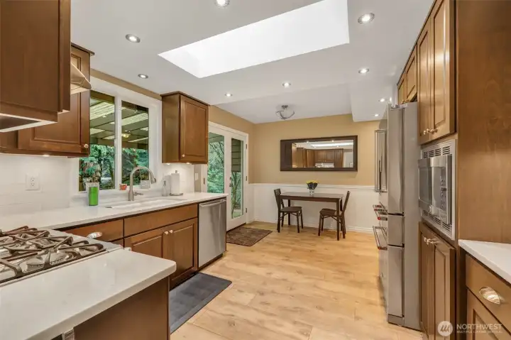 The kitchen shines with a skylight that fills the room with natural light. Rich cabinetry, sleek countertops, and stainless steel appliances create a balance of warmth and modern convenience. The space opens to a casual dining area with access to the backyard.