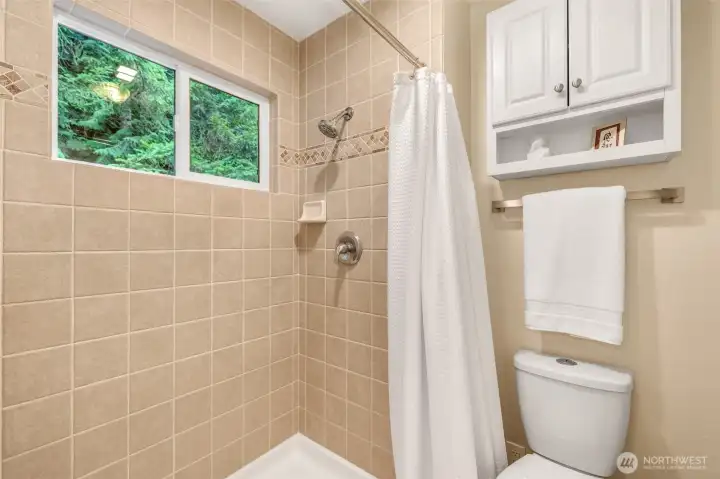 A tiled walk-in shower with a window adds to the ensuite’s appeal. Neutral tile with an accent border creates a timeless look, and the shower brings in natural light from outside.