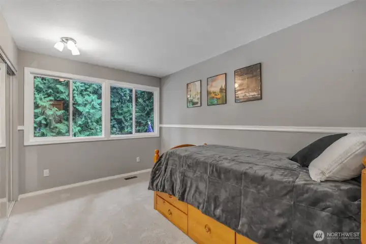 Another bedroom offers a peaceful retreat with fresh carpet and large windows that capture views of surrounding evergreens. It’s a versatile space that can easily serve as a guest room, home office, or personal hobby room.