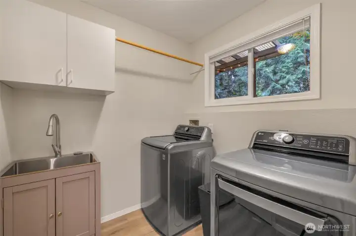 The laundry room includes full-size washer and dryer, a utility sink, overhead storage, and a window that lets in natural light. Thoughtfully designed, this space adds to the home’s practical comforts.