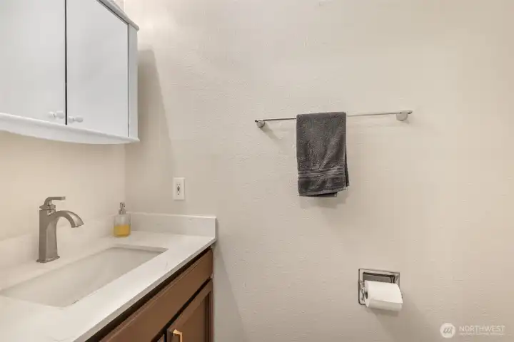 A convenient half bath on the lower level features a modern vanity with quartz countertop and updated fixtures—ideal for guests or everyday use.