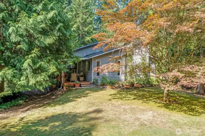 Another angle of the backyard highlights the landscaped surroundings and spacious lawn. The covered deck provides a natural gathering spot while enjoying the wooded setting.