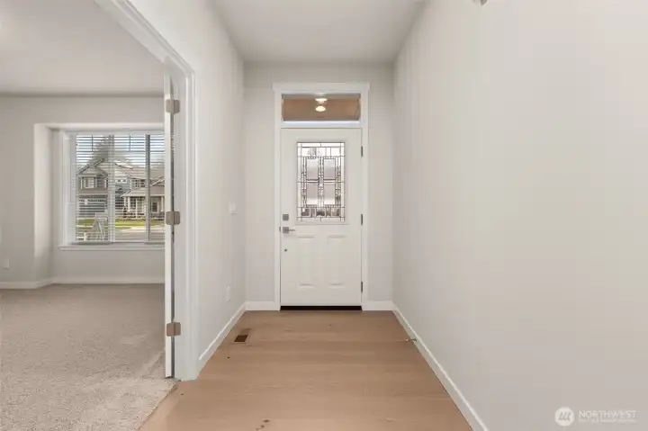 Looking toward the front door. The front door is white with a decorative glass insert and a transom window above, allowing natural light to filter in.