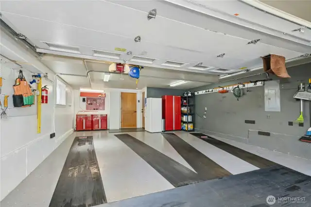 Custom epoxy chip floor, GarageTrac interlocking tile, and rubber park mats  Wi-Fi controlled LiftMaster door, retractable extension cord, and LED lighting  Gladiator and Husky cabinetry systems with solid wood counters  Dedicated workbench lighting and garage wall/car door protectors  • Mounted steel magnet board, pipe-style coat rack, pegboard, and shelving—ready for hobbyists or tinkerers