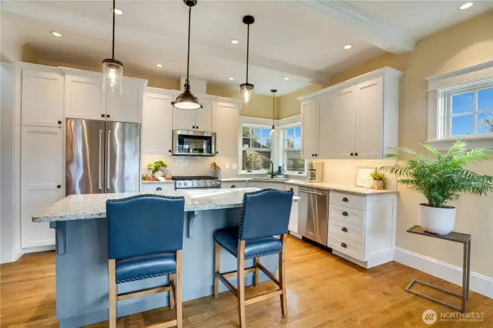 The kitchen features quartz counters, custom soft-close, shaker-style cabinetry, recessed lighting, and an island with extra seating—perfect for entertaining or a relaxing start to your day.