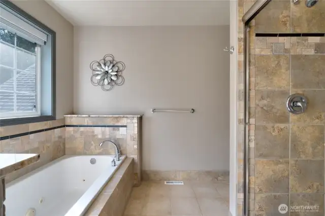 The luxurious primary bath features a soothing jetted tub and a walk-in shower enclosed by sleek glass doors, all bathed in plenty of natural light—creating a bright, spa-like retreat for relaxation and rejuvenation.