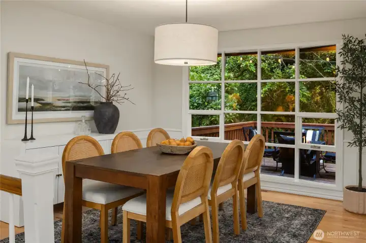 The dining room is an elegant and inviting space, featuring rich hardwood floors, new Visual Comfort lighting, and charming bay window for a distinctive architectural touch and view to the serene and lush backyard views.