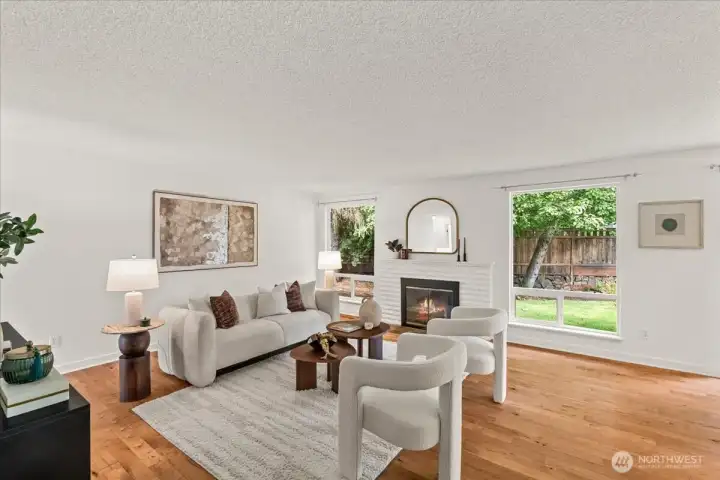 Family Room – Spacious living area with maple hardwood floors, large picture windows, and a fireplace with painted brick surround. Abundant natural light highlights the open layout.