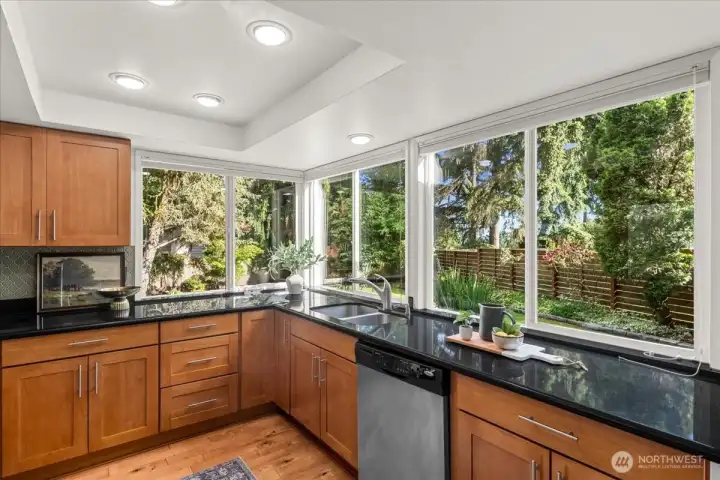 Kitchen – Well-appointed kitchen featuring wood cabinetry, granite countertops, stainless steel dishwasher, and extensive windows overlooking the yard. Abundant natural light brightens the workspace.