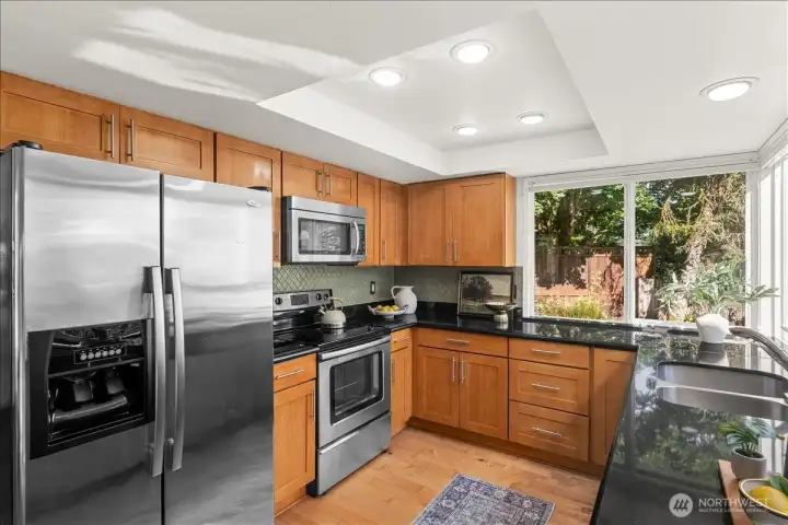 Kitchen – Functional kitchen with stainless steel appliances, granite countertops, tile backsplash, and ample cabinet storage. Large windows provide pleasant backyard views.
