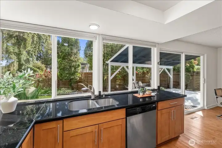 Kitchen – Kitchen sink positioned beneath expansive windows with views of the landscaped backyard and covered deck. Sliding glass doors provide easy access to outdoor living spaces.