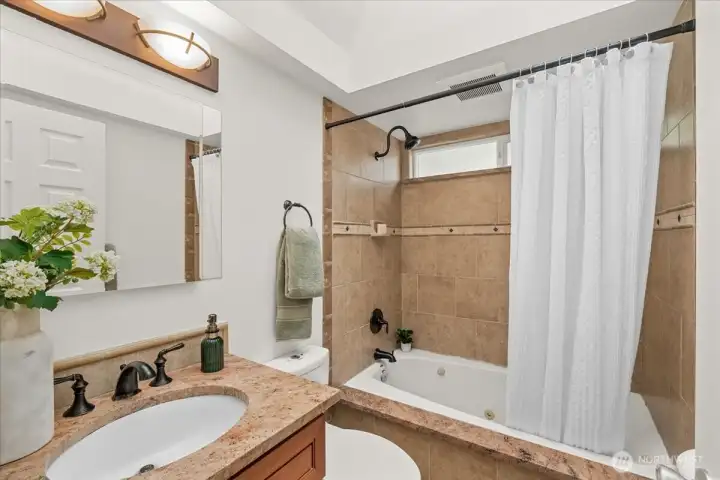 Primary Bathroom – Full bath featuring a granite-topped vanity, tile-surround tub and shower combination, and updated fixtures. Clerestory window brings in natural light while maintaining privacy.