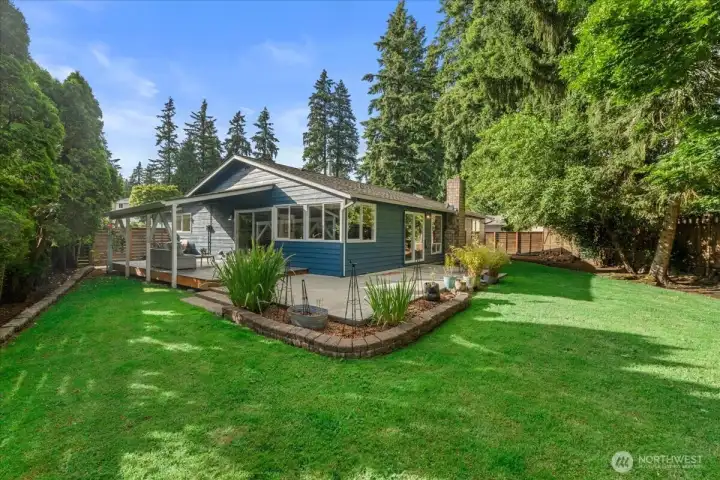 Rear Exterior – Rear view of the home showcasing the covered deck, patio, and landscaped yard. Surrounded by mature greenery for a picturesque outdoor setting.