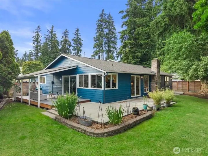 Rear Exterior – Rear exterior showcasing the covered deck, patio, expansive lawn, and mature landscaping. Designed for comfortable indoor-outdoor living and entertaining.
