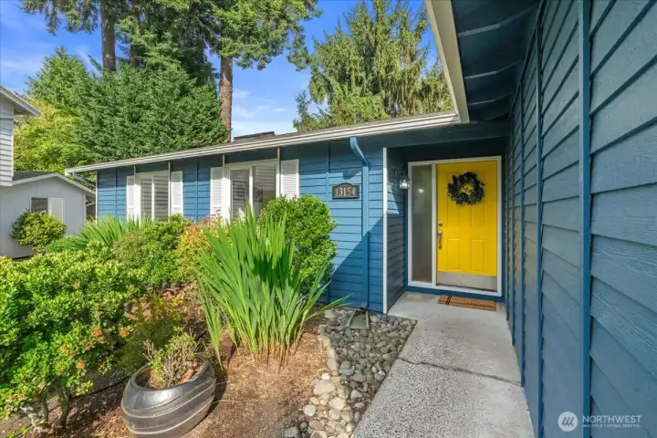 Entryway – Covered front entrance framed by colorful landscaping and decorative rock accents. Pathway leads to a distinctive front door with sidelight window.