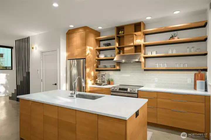 Custom kitchen features marble countertops, induction range, a walk-in pantry with appliance storage and sleek concrete floors.