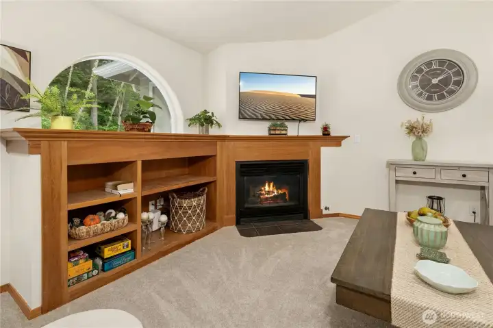 Well designed storage cabinets and arched window border cozy gas fireplace