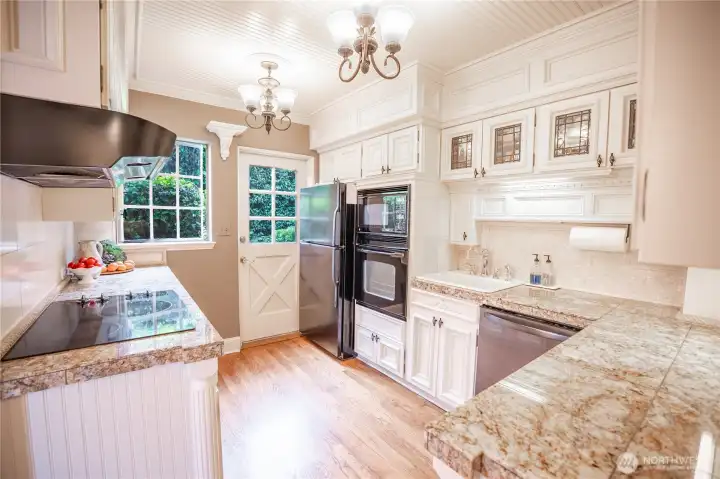 A modern kitchen outfitted with stainless appliances, white cabinetry and slabs of granite on the countertops.