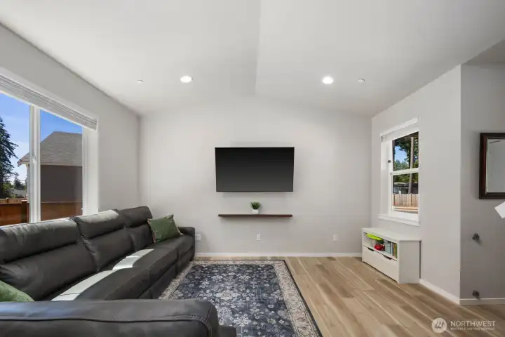 Additional view of the living area showcasing natural light, vaulted ceilings, and a wall-mounted media setup.