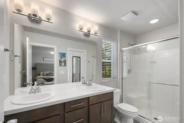Bathroom featuring a dual-sink vanity, large mirror, and glass-enclosed shower.