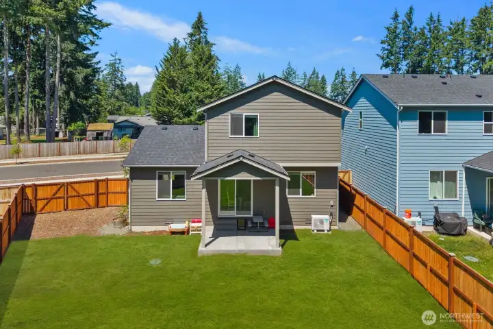 Rear exterior view showcasing the covered patio, fenced backyard, and lawn area.