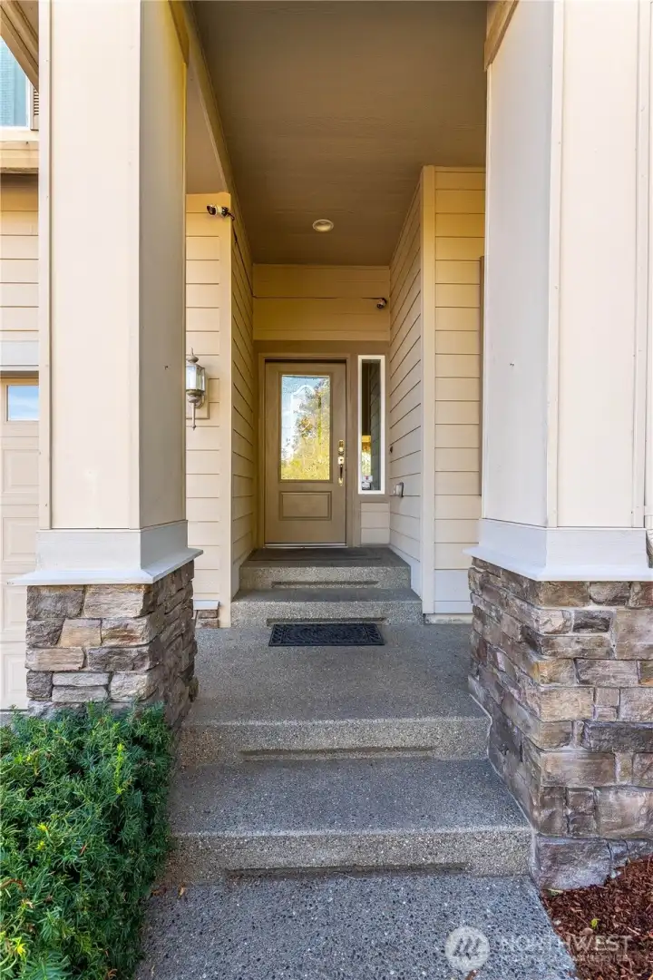 Welcome to your new home! The covered front entry makes a warm first impression with stone accents, clean lines, and a modern craftsman design. The sheltered walkway adds charm and practicality—perfect for greeting guests or staying dry on a rainy Washington day. A glass front door lets natural light into the foyer, giving a glimpse of the bright, welcoming space inside.