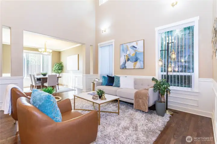 This light-filled living room brings comfort and sophistication together. The tall windows frame the outdoor greenery, while wainscoting and neutral paint tones add classic character. It’s open to the formal dining area, creating a sense of flow and space ideal for gatherings or quiet evenings at home.