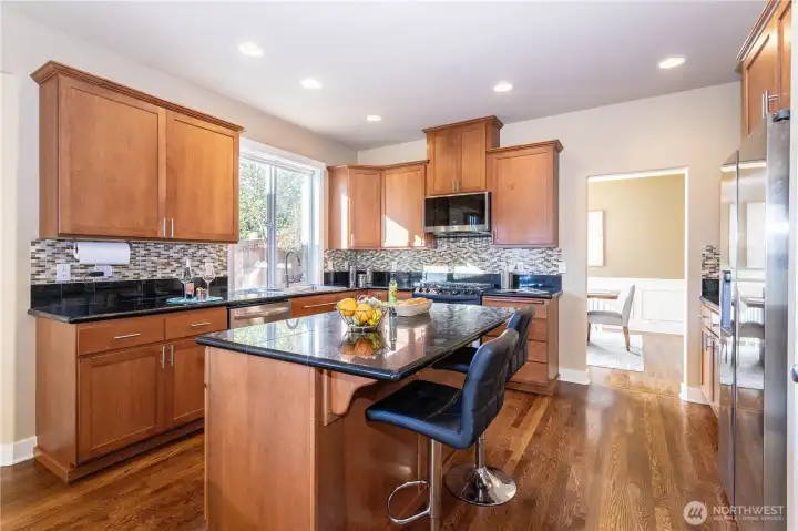 Modern kitchen featuring solid wood cabinetry, a central island with bar seating, and sleek granite counters. Stainless-steel appliances and tile backsplash elevate the design, offering both beauty and function.