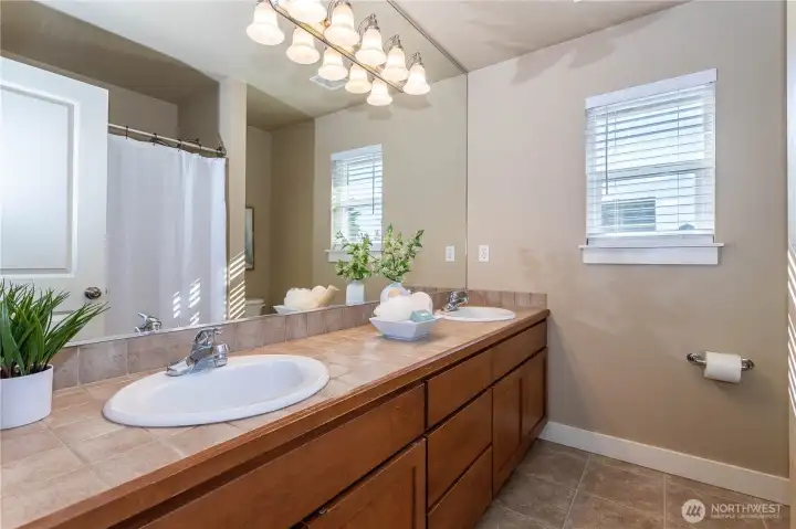 Stylish full bath featuring dual sinks, wide vanity, and tile countertops. A full-size tub and shower combination, soft lighting, and natural-toned finishes create a clean, relaxing atmosphere. Perfectly located to serve the upstairs bedrooms and loft.